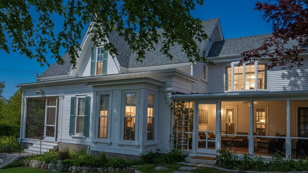 A two-story house with a covered porch and a large window overlooking the yard.