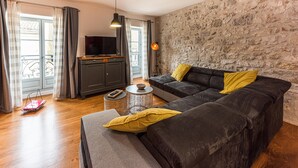 A living room with a stone wall, a dark sofa with yellow pillows, a television on a wooden cabinet, and a wicker coffee table.