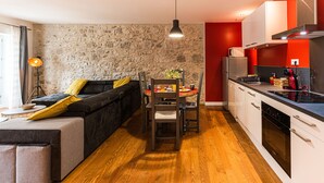 A modern kitchen with a stone wall, wooden flooring, and a dining area with a table and chairs.