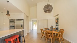 Une cuisine moderne équipée d’appareils électroménagers en acier inoxydable, une table à manger en bois avec des chaises, et un tabouret de bar rouge.