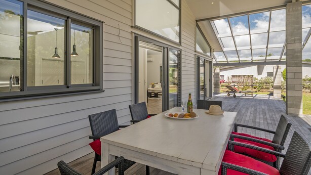 Une terrasse couverte avec une table blanche et des chaises rouges, de grandes fenêtres et une vue sur le jardin arrière.