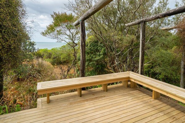 Un banc en bois sur une terrasse donnant sur une plage, avec une végétation luxuriante et un ciel dégagé.