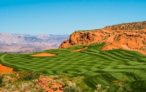 A golf course with sand bunkers and a mountainous backdrop.
