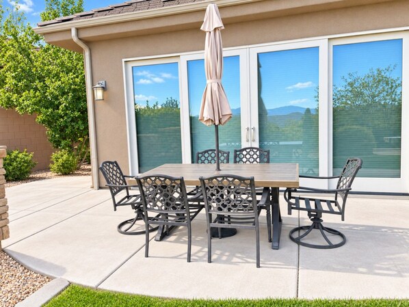 An outdoor patio with a table and chairs, a covered umbrella, and a view of a building with large windows.