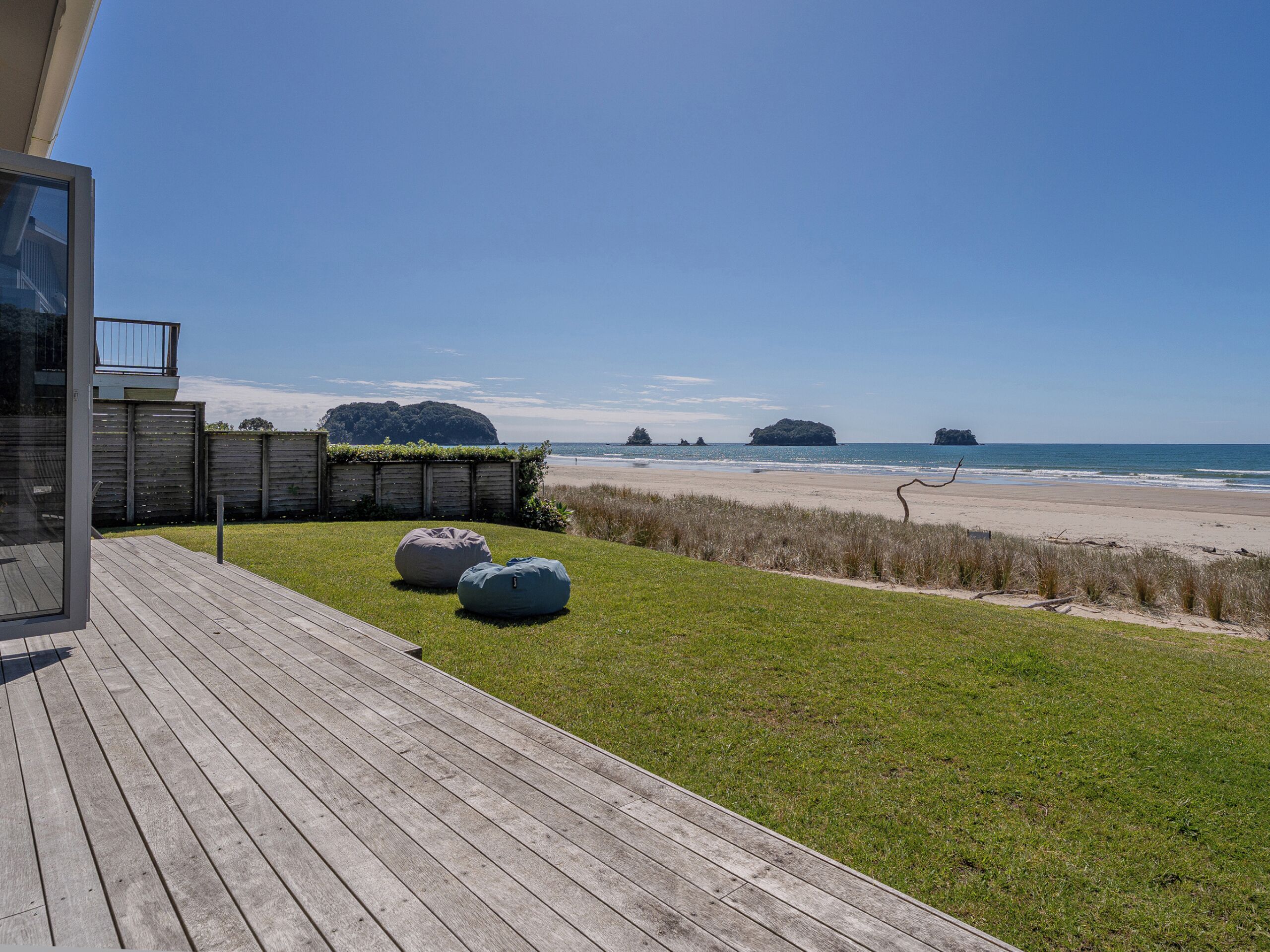 Une terrasse en bois avec deux fauteuils en forme de sac de haricots, une zone herbeuse et une vue sur la plage, avec des îles qui se dessinent à l'horizon.