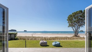 A beach view from a deck with a wooden floor, two bean bags, and a tree. - Beachfront Beauty - Whangamata Beachfront Home (Whangamata)