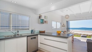 A modern kitchen with a dishwasher, a large island, and a view of the beach. - Beachfront Beauty - Whangamata Beachfront Home (Whangamata)