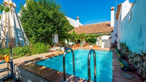 Una piscina con cubierta de piedra, rodeada de abundante vegetación y edificios blancos con tejados de teja.