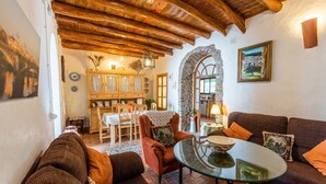 Una sala de estar acogedora con muebles de madera, una mesa de centro de vidrio y un arco de piedra que da a una cocina.