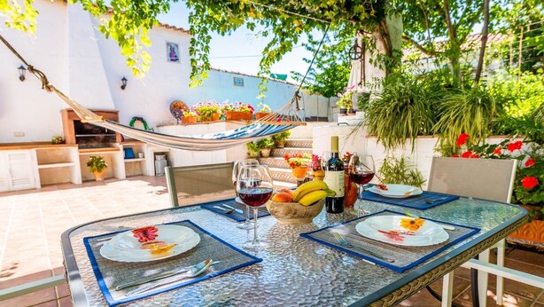 Un área de comedor al aire libre con una mesa de vidrio, sillas y una hamaca.
