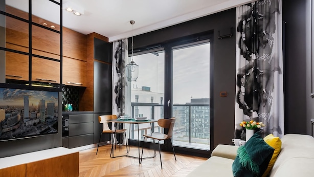 A modern living room with a large window, a dining area, and a TV mounted on the wall.