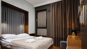 A modern hotel room with a wooden bed, a small desk, and a window with blinds.