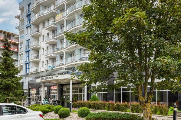 A multi-story hotel with a spa, a covered entrance, and a parking area with a white car. - Distinctive Apartment | Balcony, 300 m to the Beach (Kolobrzeg)