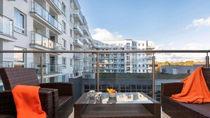 A balcony with wicker furniture, a glass table, and a view of modern apartment buildings.