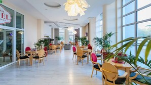 A spacious indoor area with multiple round tables and chairs, large windows, and hanging paper lamps.