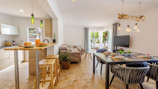 A modern kitchen with a dining area, a sofa, and a TV.