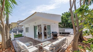 A modern house with a patio area featuring outdoor furniture, a barbecue, and a view of the backyard.