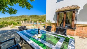 A patio with a table and chairs, a bottle of wine, and a view of a hillside. - Los Linarejos Ronda by Ruralidays (Málaga)