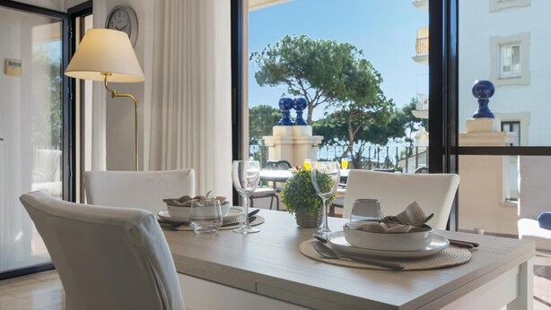 A dining area with a table set for two, a lamp, and a view of the sea and buildings. - Apartment in Andalucía del Mar for 2 people | ADM 10-107 (Puerto Banús - Marbella)