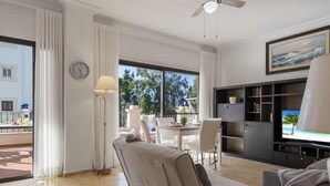 A modern living room with a sofa, a dining table with chairs, a TV, and a ceiling fan. - Apartment in Andalucía del Mar for 2 people | ADM 10-107 (Puerto Banús - Marbella)