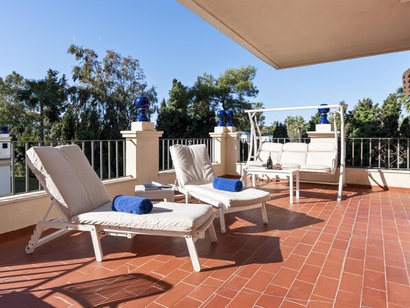 A sunlit outdoor seating area with two lounge chairs, a small table, and a decorative blue vase.