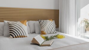 A neatly made bed with white bedding and striped pillows, a book, and a small plant on the bed.