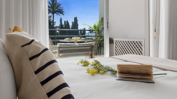 A balcony with a table and chairs, a view of palm trees, and a door leading to an outdoor area.