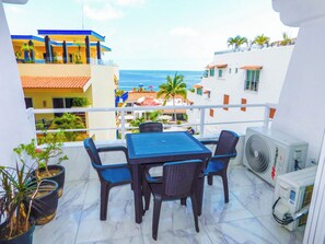 Ein Balkon mit Tisch und Stühlen, der Blick auf das Meer und Gebäude bietet.