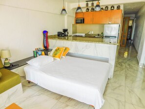 Ein Hotelzimmer mit einem Bett, einem Nachttisch, einer Lampe, einem Sessel, einem kleinen Tisch, einer Mikrowelle, einem Kühlschrank und einer Küchenzeile mit Schränken und einer Arbeitsplatte.