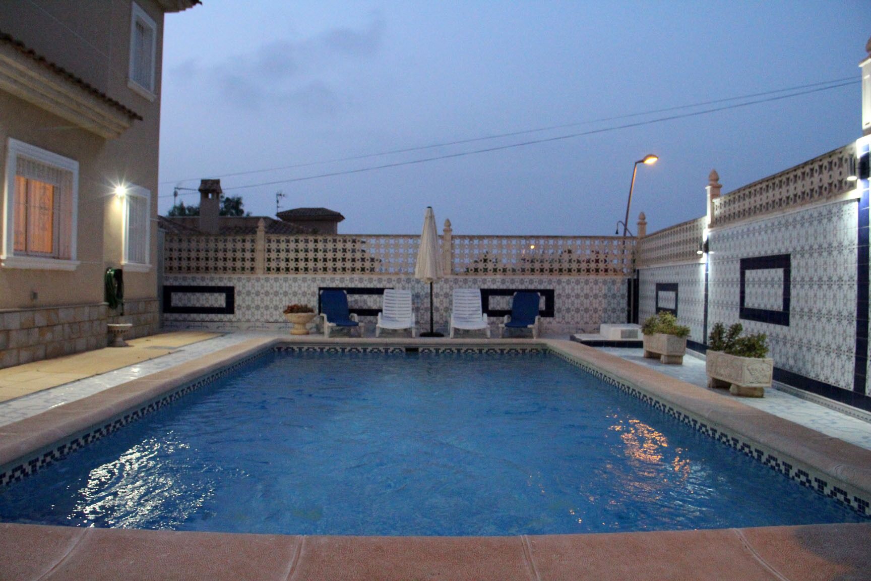 Ein Pool mit gefliesten Wänden, zwei Liegestühlen und einem Tisch mit einer Pflanze.