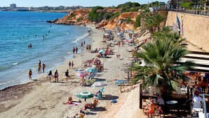 A beach with people swimming and sunbathing, umbrellas, and outdoor seating areas.