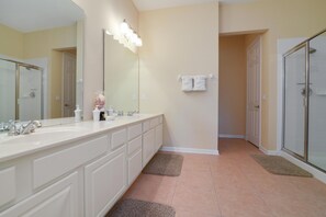 A bathroom with a large mirror, two sinks, a shower, and a towel rack.