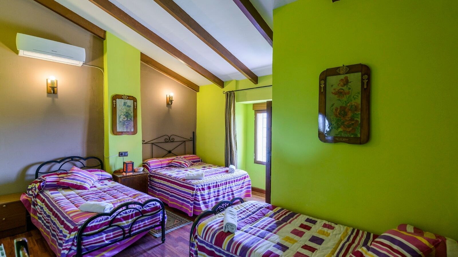 Habitación con dos camas, cada una con ropa de cama a rayas, un ventilador de techo y un aire acondicionado instalado en la pared.