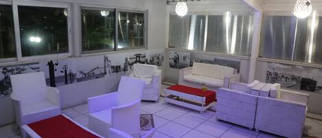 A room with white wicker furniture, a red cushion, and a tiled floor.