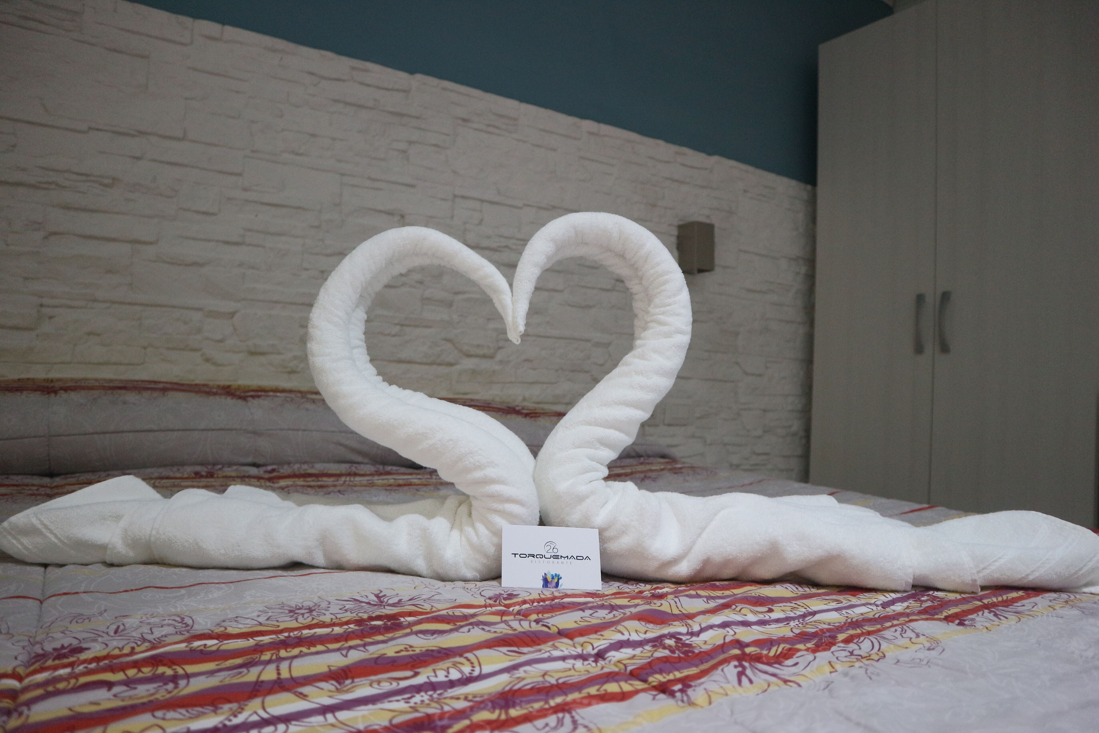 A bed with a heart-shaped towel arrangement and a sign reading "TORQUEMADA".