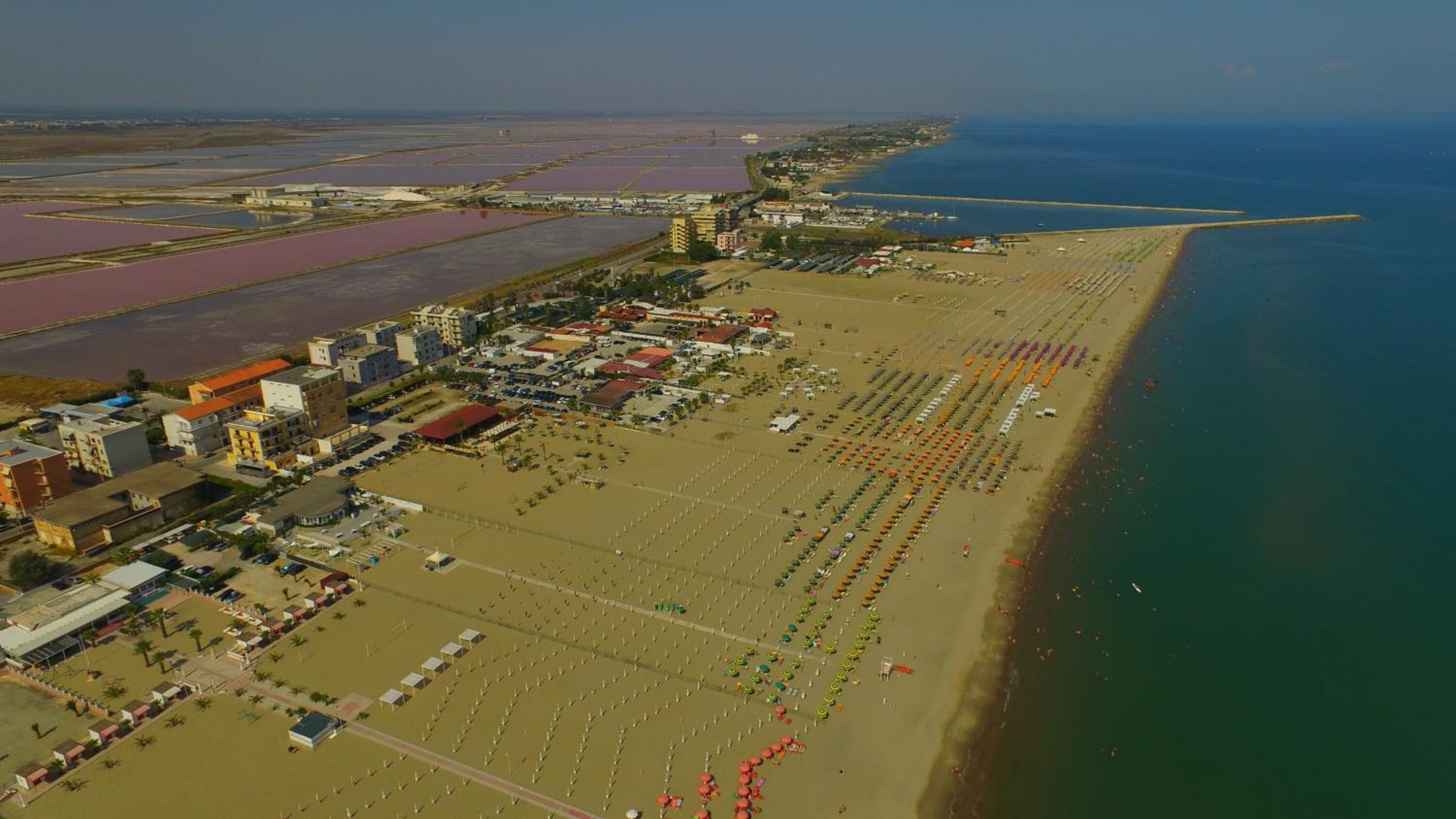 Vista aérea de una zona costera con playa, estacionamientos y edificios.