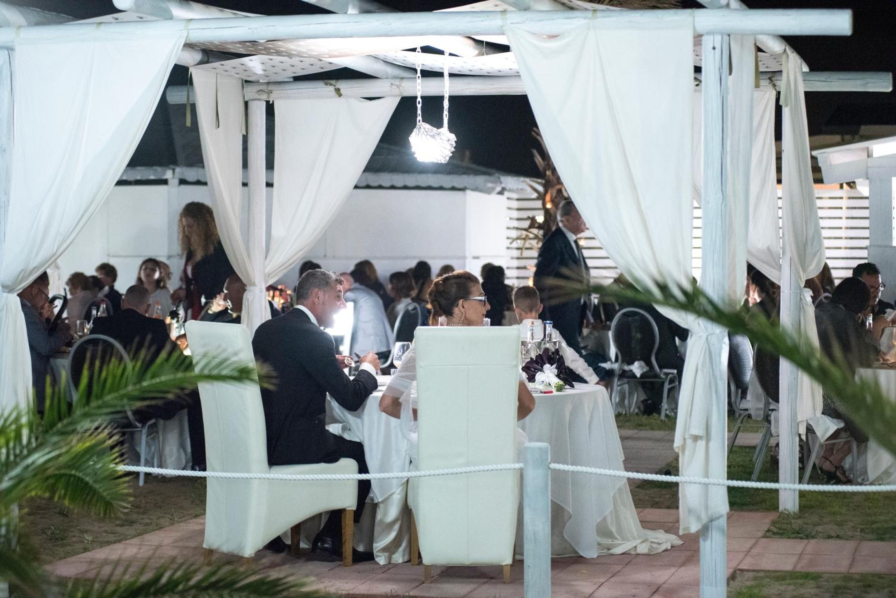 Una recepción de boda al aire libre con carpas y mesas blancas.