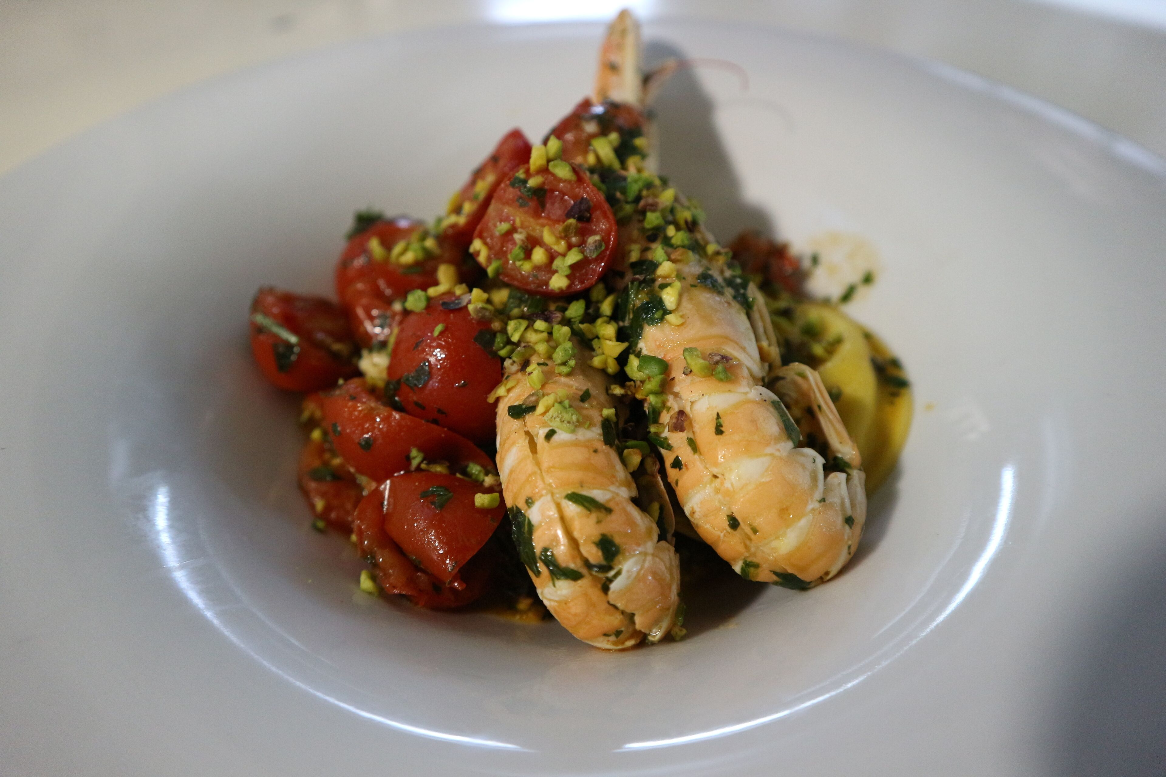 Un piatto con una coda di aragosta, pomodorini ciliegino ed erbe aromatiche tritate.