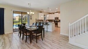 A spacious kitchen with a dining area, a staircase, and a view of a backyard. - Cool Breeze by VillaDirect (Davenport)