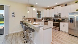 A modern kitchen with white cabinets, stainless steel appliances, and a bar area with stools. - Cool Breeze by VillaDirect (Davenport)