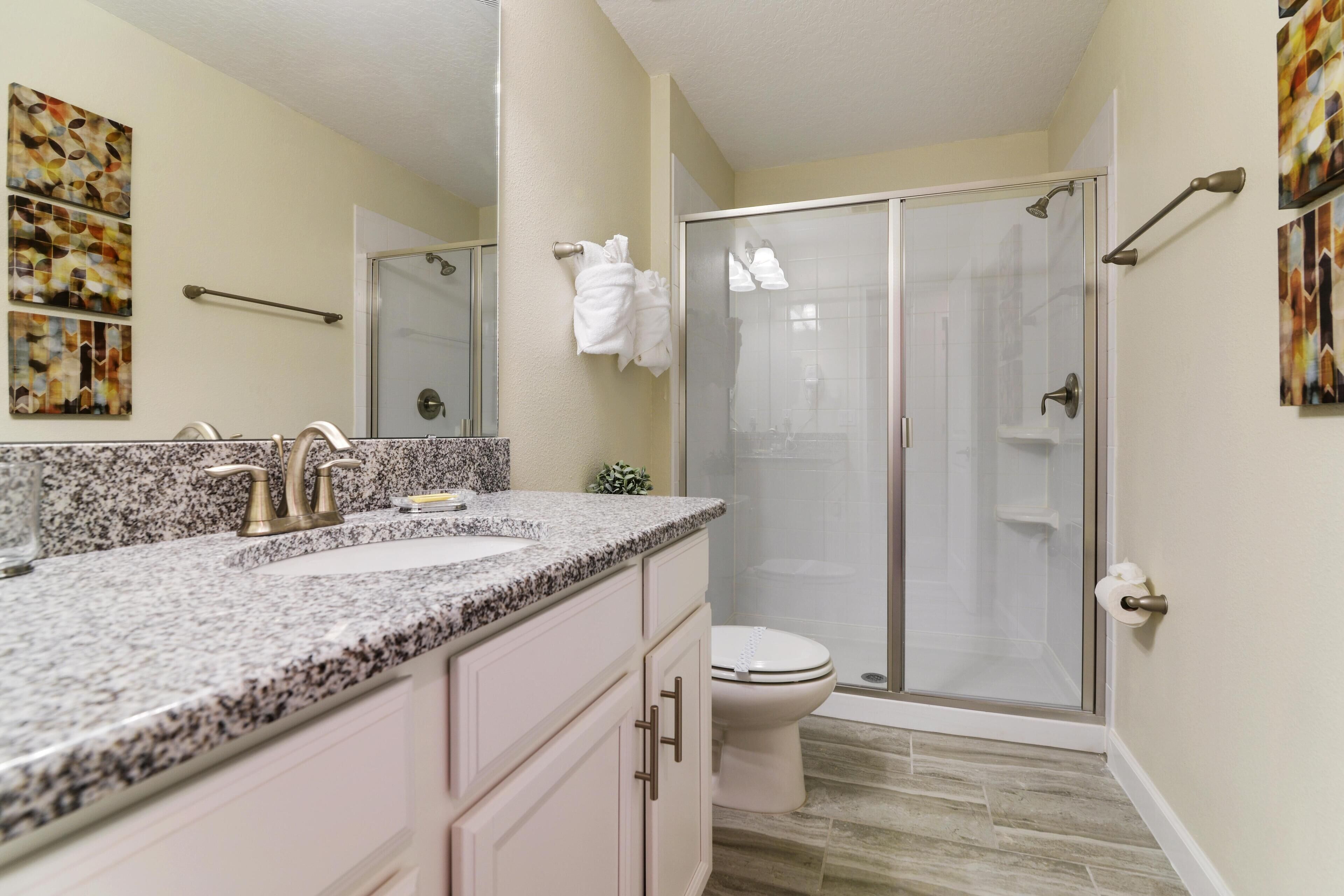 A bathroom with a granite countertop, two sinks, a toilet, and a glass-enclosed shower.
