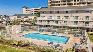A hotel with a swimming pool surrounded by a white fence, multiple balconies, and a parking lot in the background. - 4 br townhouse ocean front, at 47th St, has outdoor pool! Lovely, with multiple oceanfront decks. (Ocean City)
