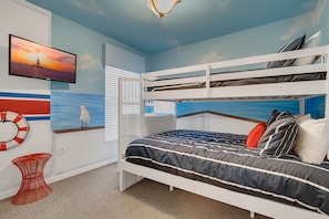Habitación con literas, un televisor, un mural con vista al mar y una silla roja.
