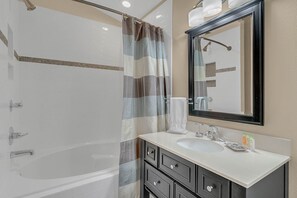 A modern bathroom with a bathtub, a large mirror, and a vanity with a sink.