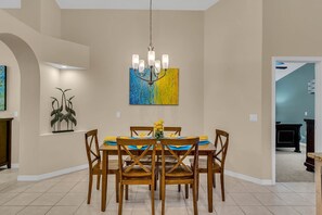 Un comedor con candelabro, una mesa dispuesta para cuatro personas y un cuadro abstracto colorido en la pared.