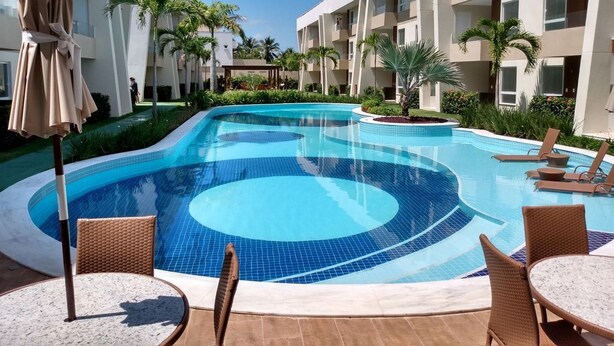 Una piscina con lettini e ombrelloni, circondata da un edificio moderno con balconi.