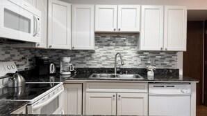 A modern kitchen with white cabinets, a black countertop, a microwave, a coffee maker, and a dishwasher.