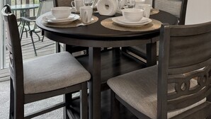 A dining area with a round table set for four, chairs, a vase with decorative feathers, and a framed picture on the wall.