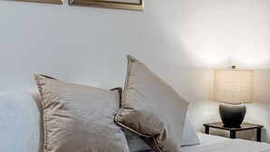 A bedroom with a bed, two pillows, a nightstand with a lamp, and two framed artworks on the wall.