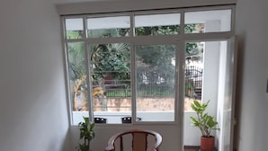 A room with a large window, two wooden chairs, a table, and a potted plant. - Rincon de Granada (Cali)
